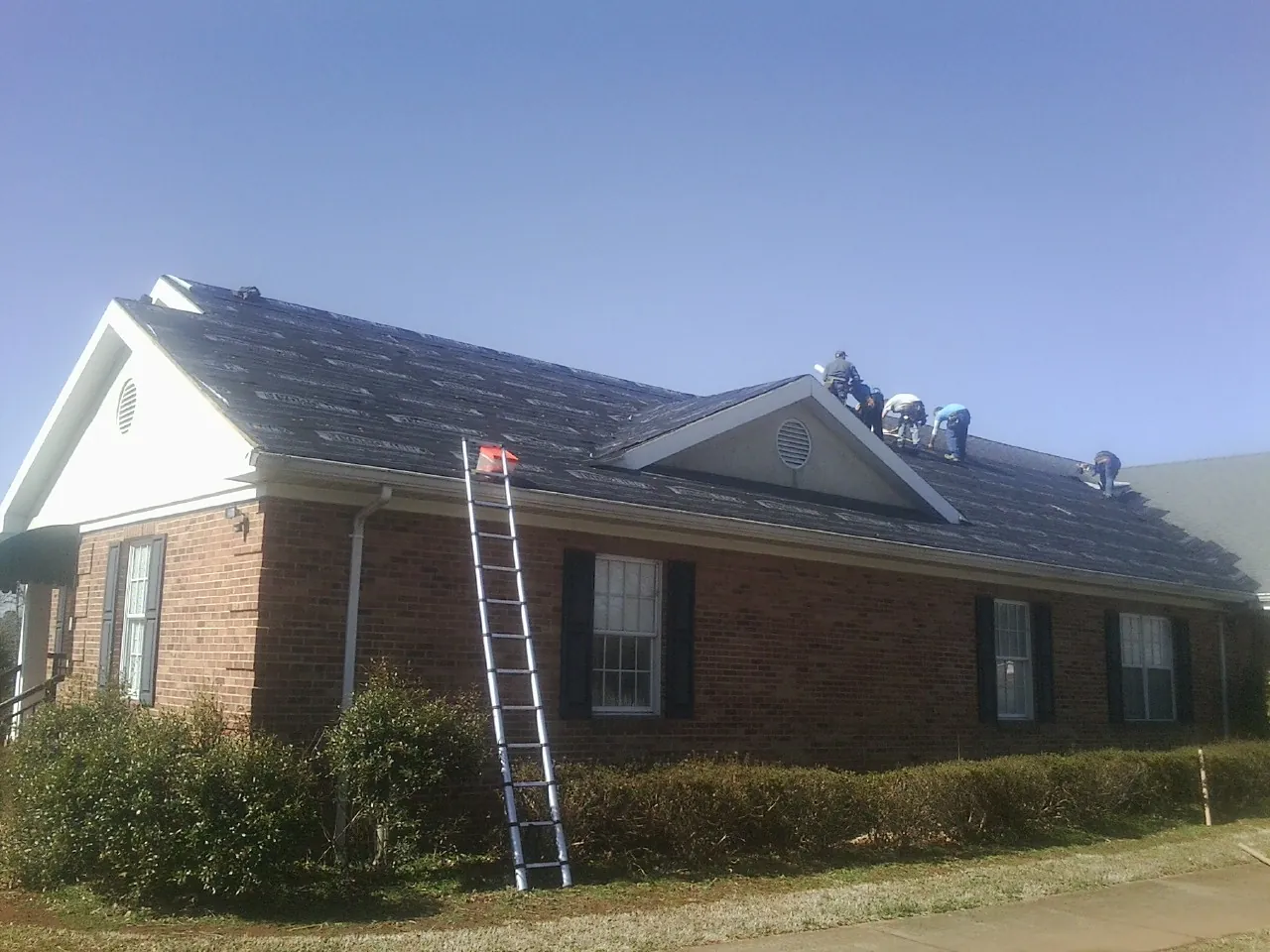 Crew tearing shingles off a brick ranch roof with a ladder set — Emergency Roof Repair work by our crew in Powder Springs