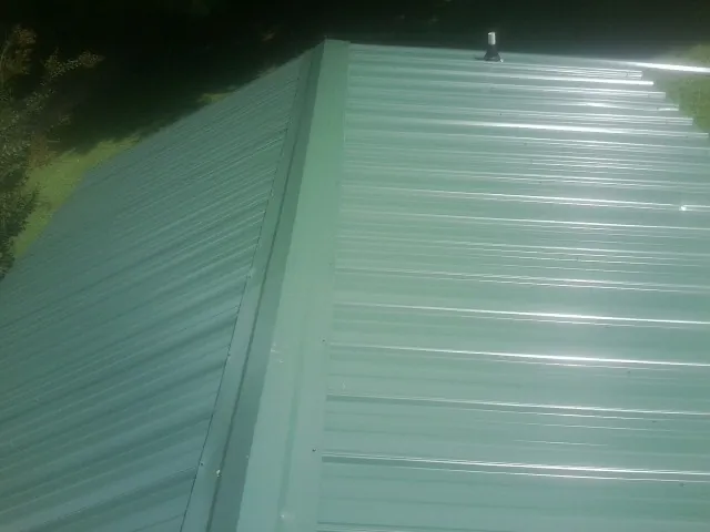 New green metal panels meeting at the ridge of a roof — Flat Roof Repair work by our crew in Powder Springs