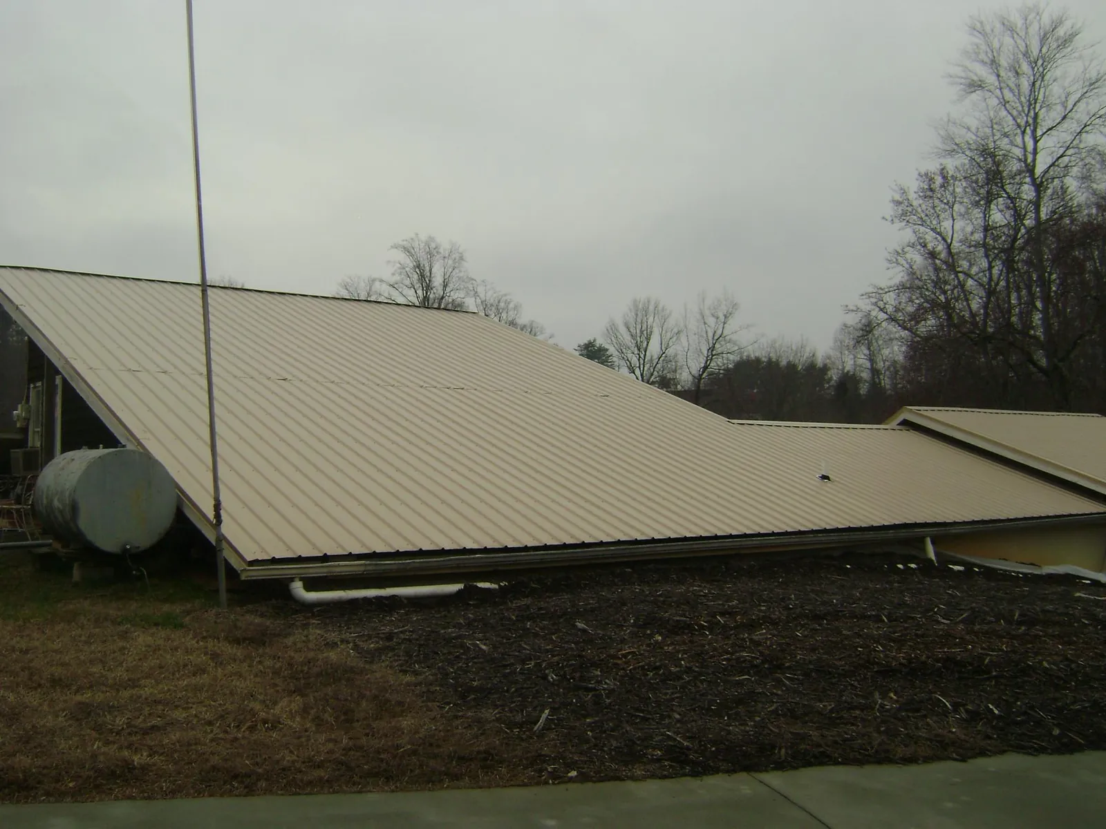 Wide tan metal roof plane seen from the ground beside a propane tank in Powder Springs