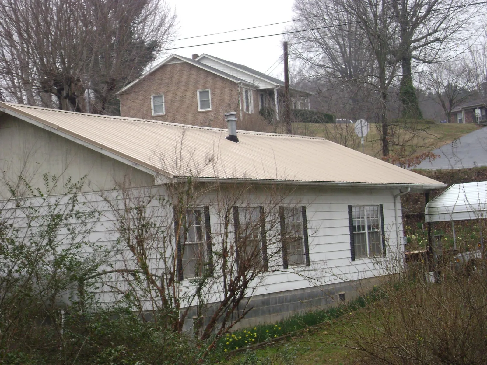 Tan metal roof on a white sided house set into a hillside — Commercial Roofing by Roofing Brothers in Powder Springs